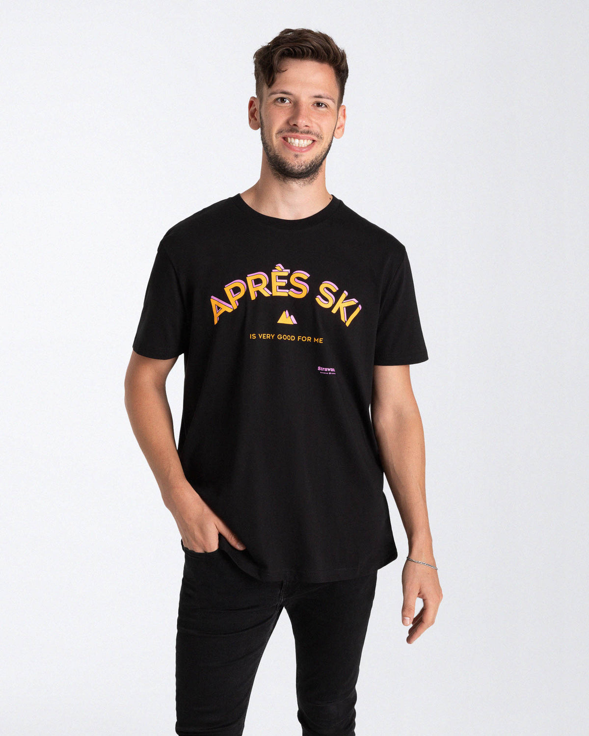 Ein männliches Model trägt ein schwarzes T-Shirt mit einem orange, rosa "APRÈS SKI IS VERY GOOD FOR ME" Schriftzug besteht und einem kleinen Berg in der Mitte der Brust.
