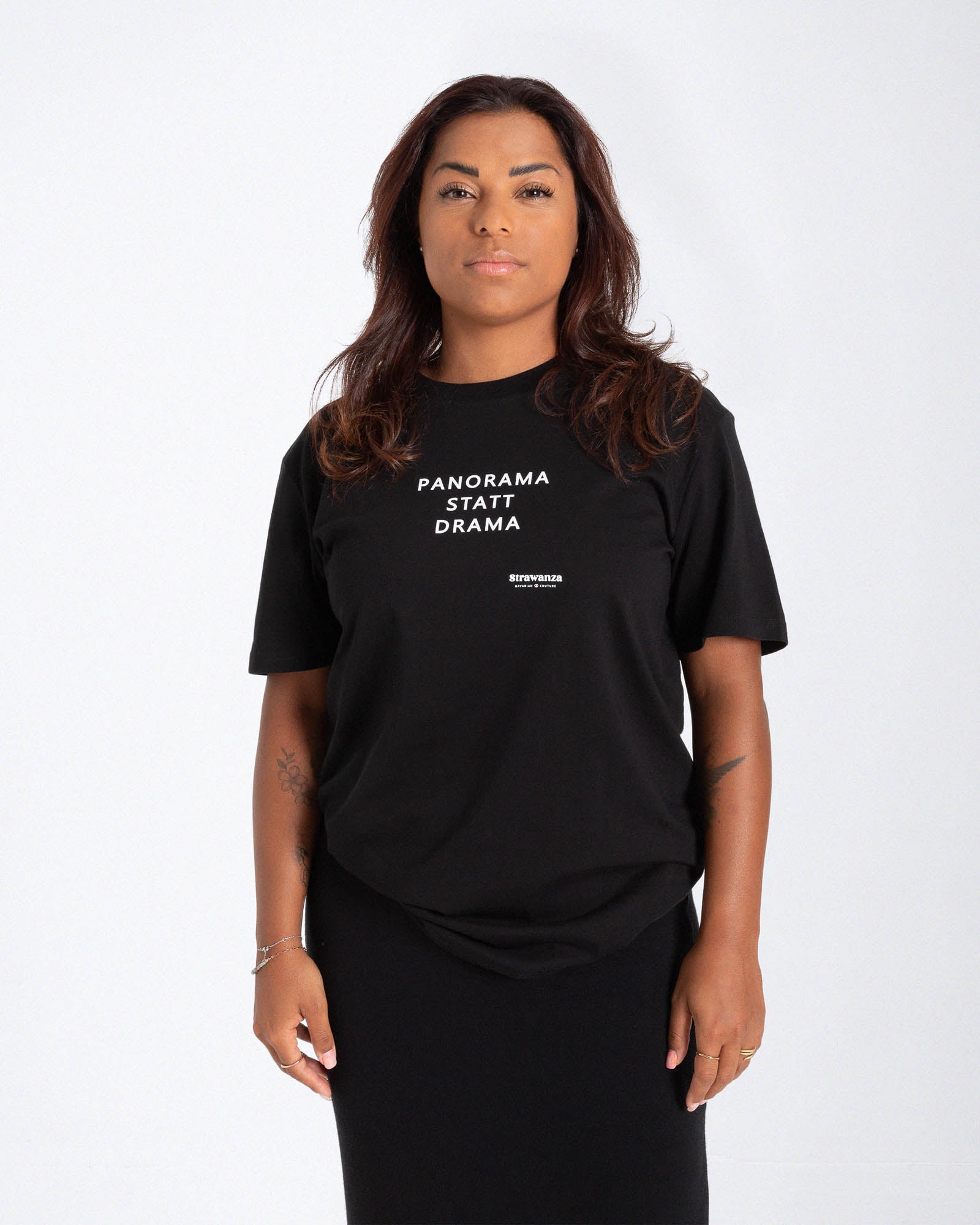 Eine Frau trägt ein schwarzes T-Shirt mit einer weißen Schrift in Höhe der Brust vor einem weißen Hintergrund. 