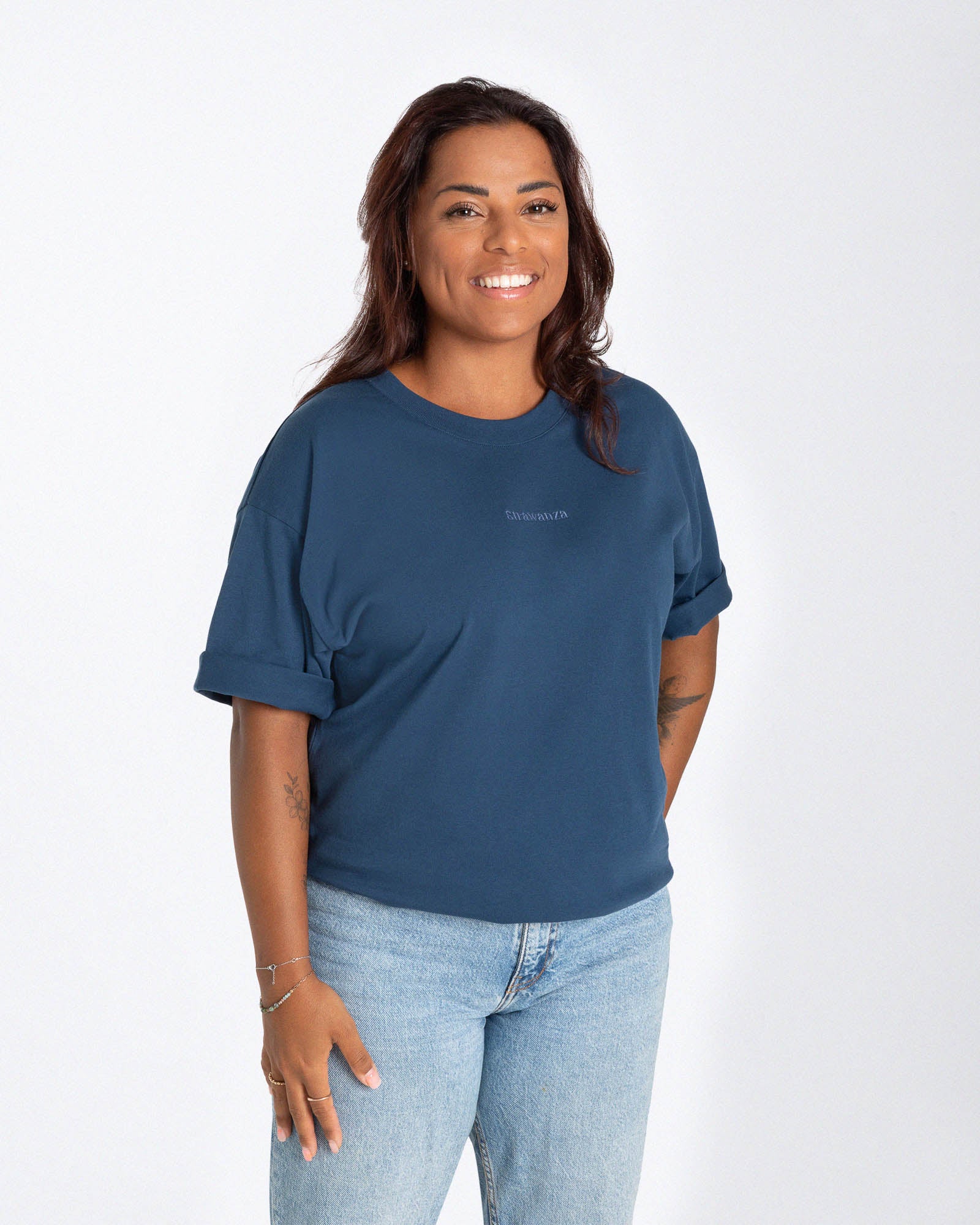 Weibliches Model trägt ein blaues T-Shirt mit einem in Ton in Ton gesticktem "Strawanza" inmitten der Brust. 