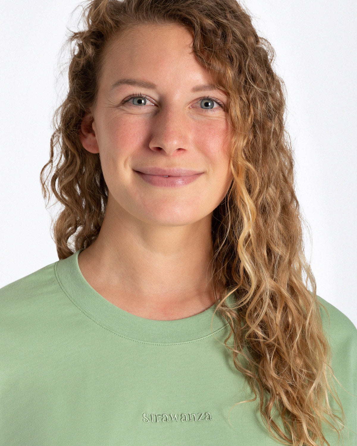 Ein weibliches Model trägt ein hellgrünes T-Shirt mit einem grünen Schriftzug auf Höhe der Brust.