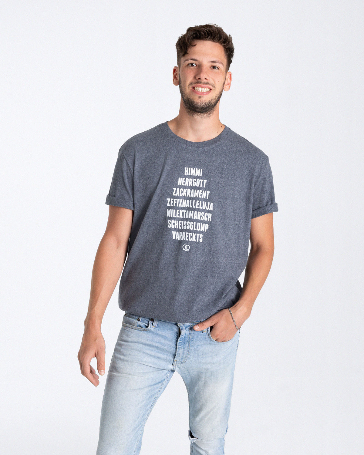 Ein männliches Model trägt ein Vintage blaues T-Shirt mit einem Print auf der Vorderseite der aus einem weißem "HIMMI HERRGOTT ZACKRAMENT ZEFIXHALLELUJA MILEXTAMARSCH SCHEISSGLUMP VARRECKTS" Schriftzug und einem weißem Breznherz besteht.