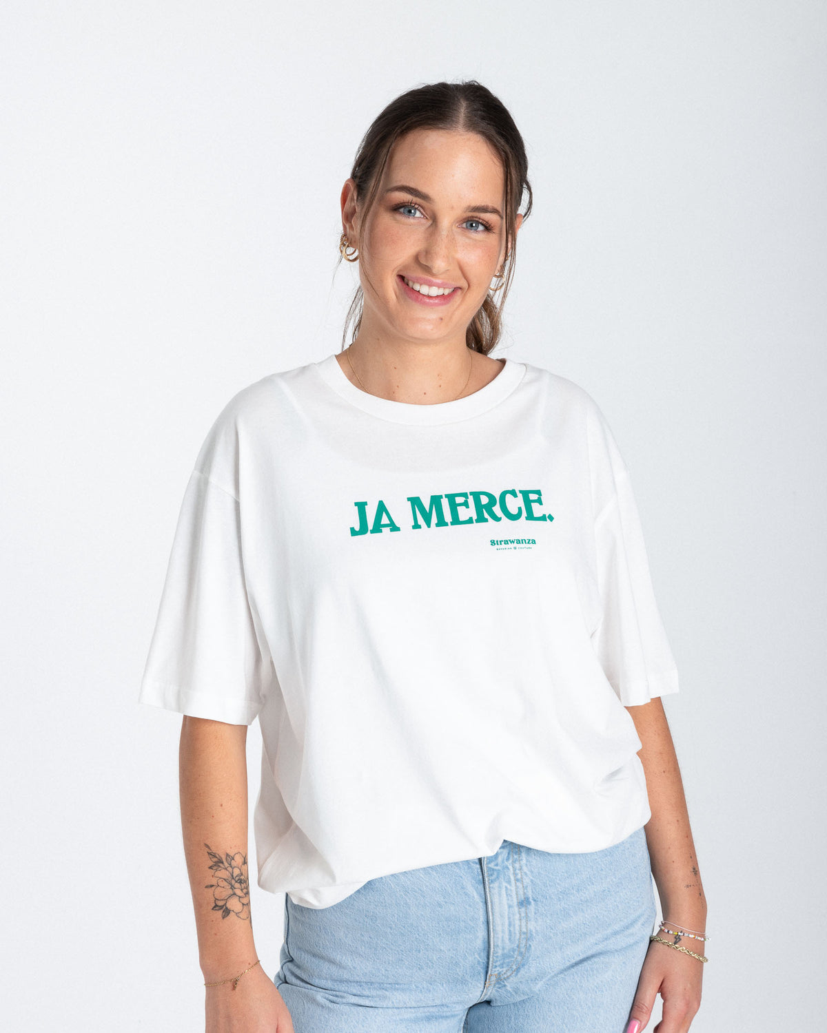 Ein weibliches Model trägt ein weißes T-Shirt mit einem dunkelgrünen, bedruckten "JA MERCE" Schriftzug auf der Höhe der Brust.