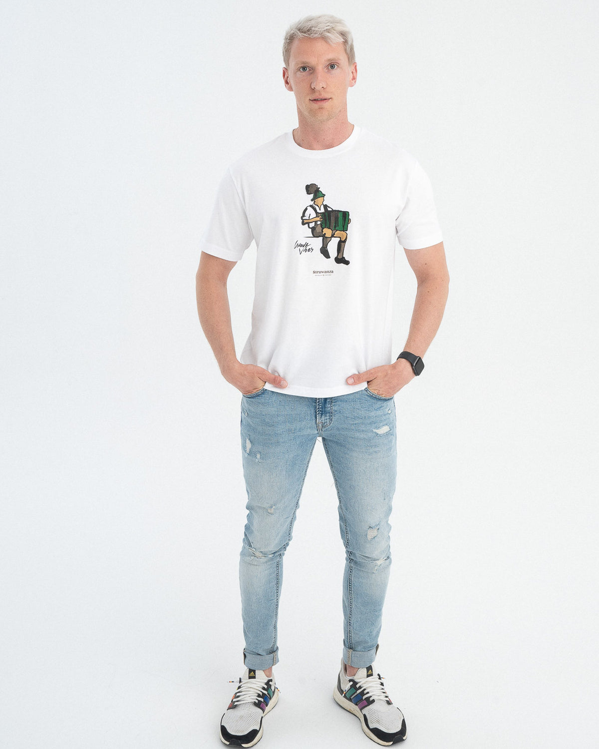 Ein männliches Modelträgt ein weißes T-Shirt mit einem Mann der Akkordeon spielt, auf der Höhe der Brust, ebenfalls ist ein schwarzer "Guade Vibes" Schriftzug als Vordermotiv drauf.