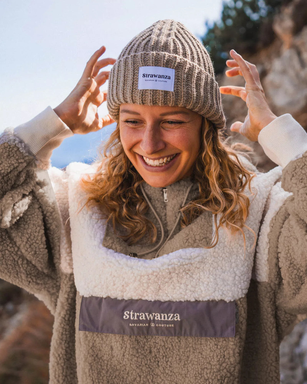 Ein weibliches Model trägt einen Sherpa Fleece Anorak in Beige, wo vorne beim Bauch eine Tasche ist um seine Wertsachen zu verstauen. 
