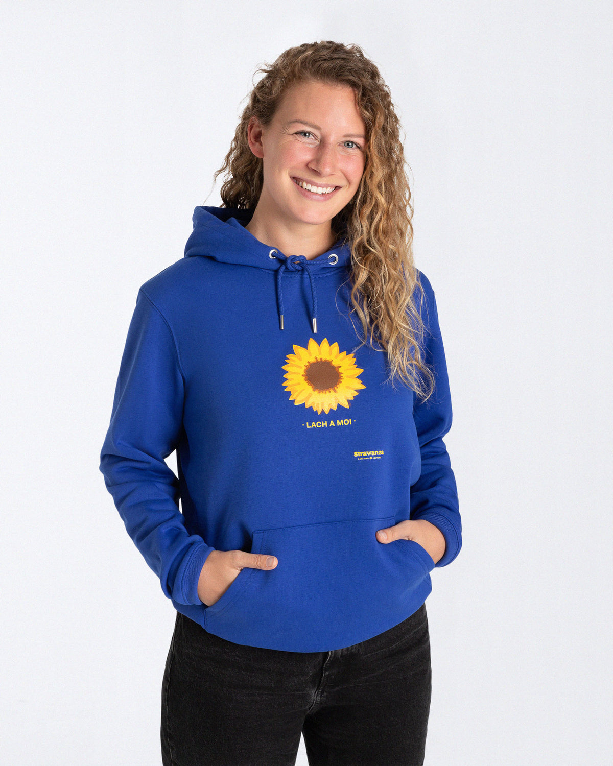 Ein weibliches Model trägt einen blauen Hoodie mit einem Motiv, dass aus einer Sonnenblume und einem gelben "LACH A MOI" Schriftzug besteht, welches auf der Höhe der Brust platziert ist.