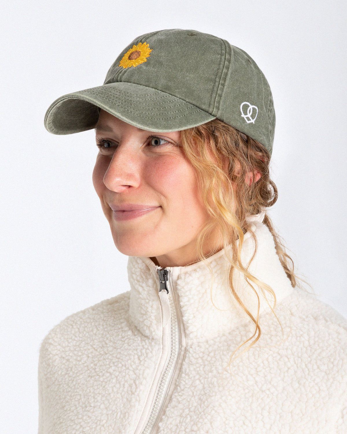 Ein weibliches Model trägt eine Bavarian Cap in der Farbe Vintage Khaki und als Motiv ist auf der Vorderseite eine Sonnenblume zu erkennen und an der Seite ein Brezn-Herz Logo in weiß gestickt.