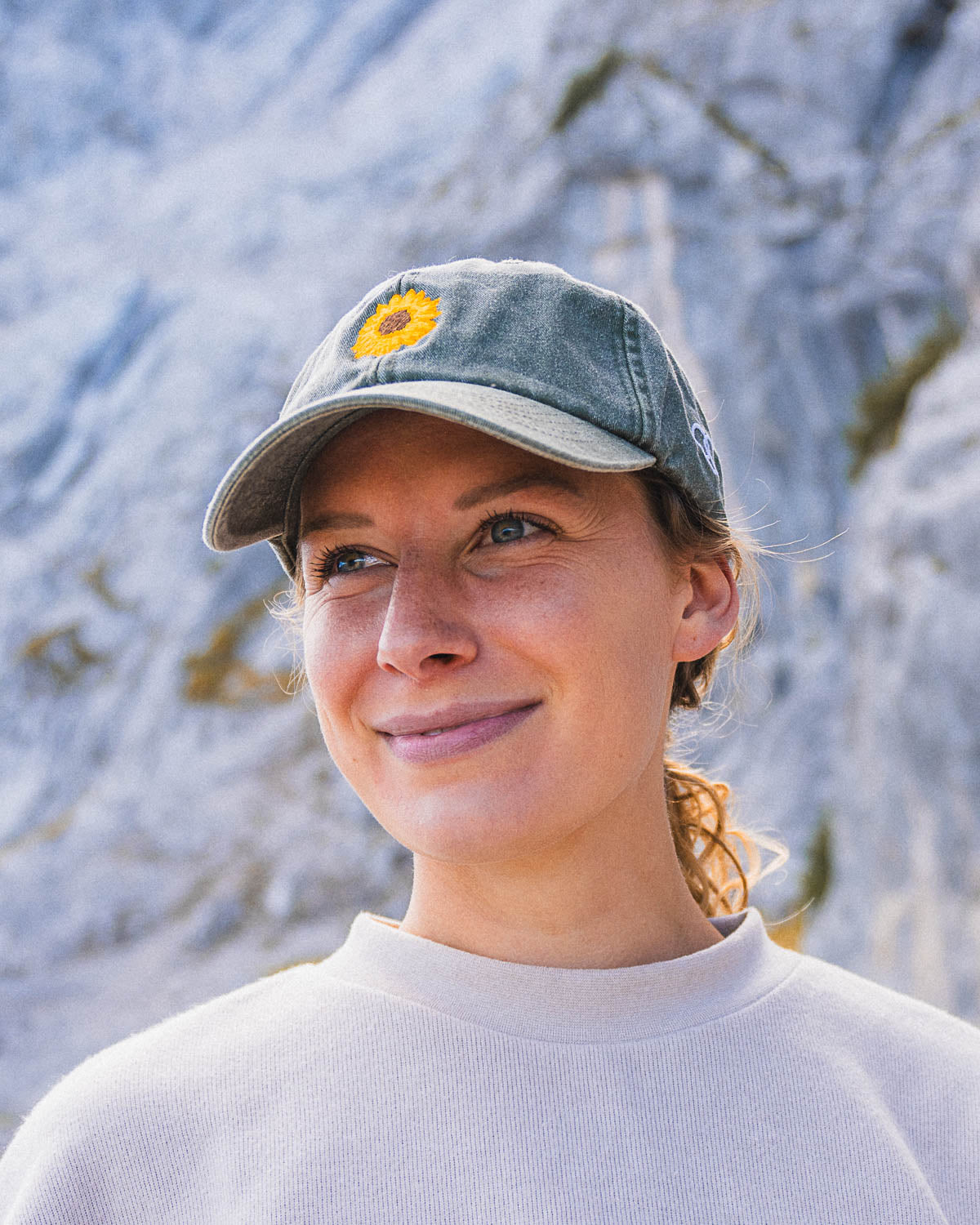 Ein weibliches Model trägt eine bayerische Cap in der Farbe Vintage dunkelgrau mit einer Sonnenblume vorne als Motiv zu erkennen.