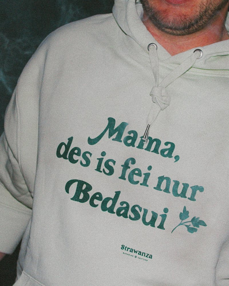 Ein männliches Model trägt einen apfelgrünen Hoodie welcher mit einem dunkelgrünen "Mama, des is fei nur Bedasui" Schriftzug versehen ist.
