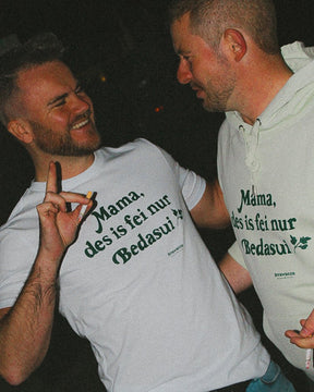 Zwei Männer tragen jeweils ein weißes T-Shirt  und einen hellgrünen Hoodie mit einem dunkelgrünen "Mama, des is fei nur Bedasui" Schriftzug vorne auf der Brust. 