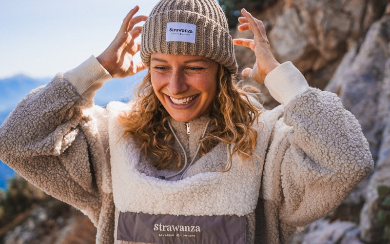 Blonde junge Frau trägt einen beigen Sherpa Fleece Anorak in den Bergen.