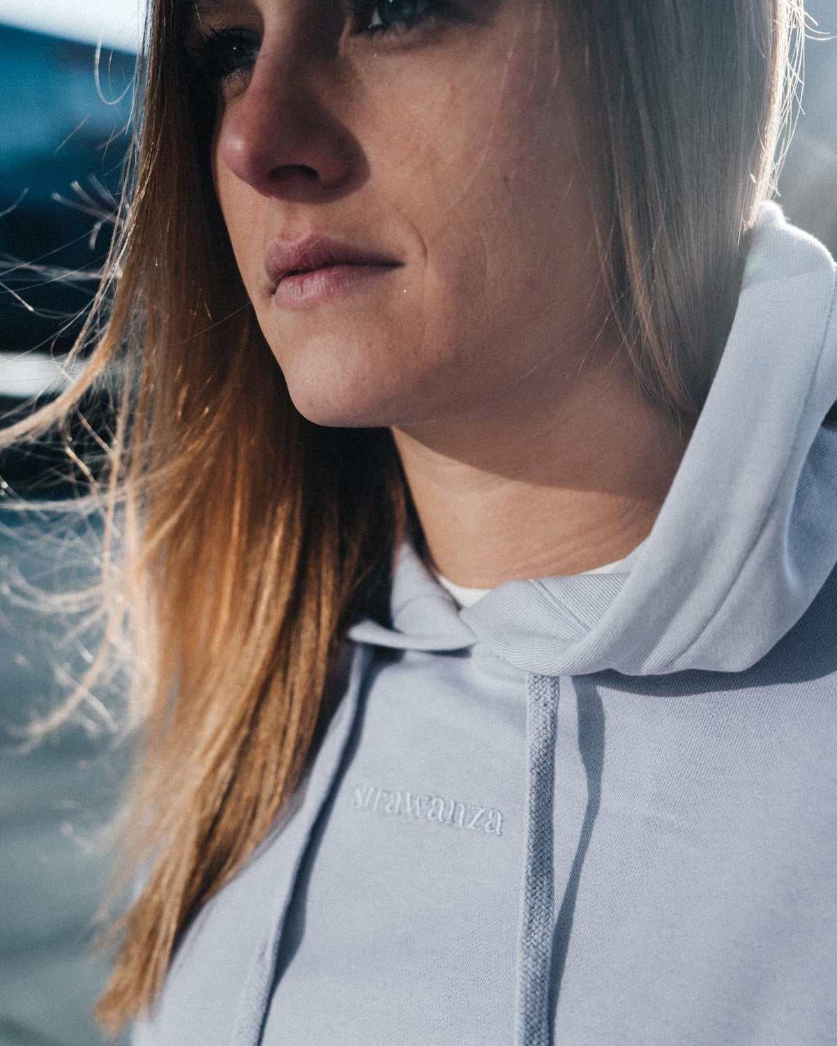 Ein weibliches Model trägt einen Fliederfarbenen Hoodie mit einem in Ton in Ton gesticktem "Strawanza" Schriftzug.