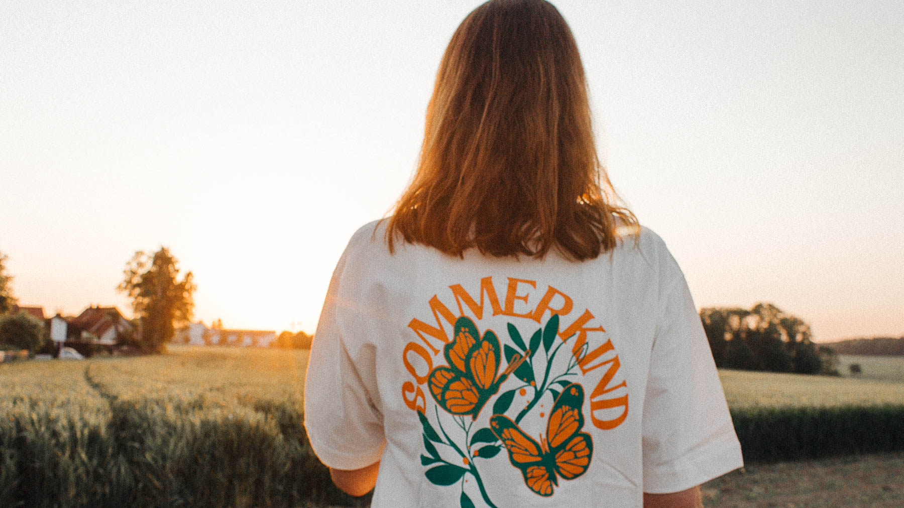 Junge Frau vor Sonnenuntergang mit einem T-Shirt von Strawanza mit dem Aufdruck "Sommerkind"