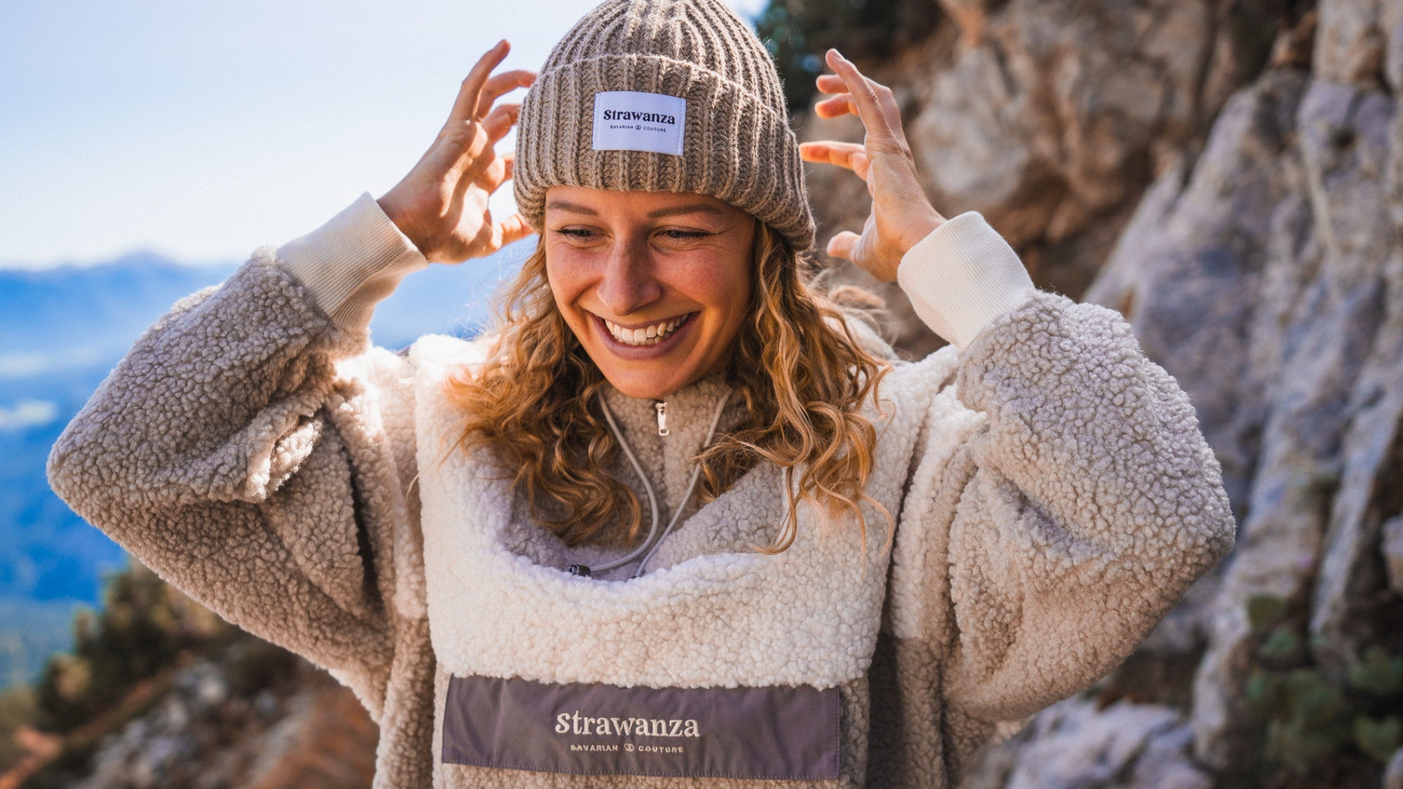 Fleece Sherpa in Beige von der bayerischen Marke Strawanza® Bavarian Couture getragen von blondem weiblichen Model in einer Berglandschaft. 