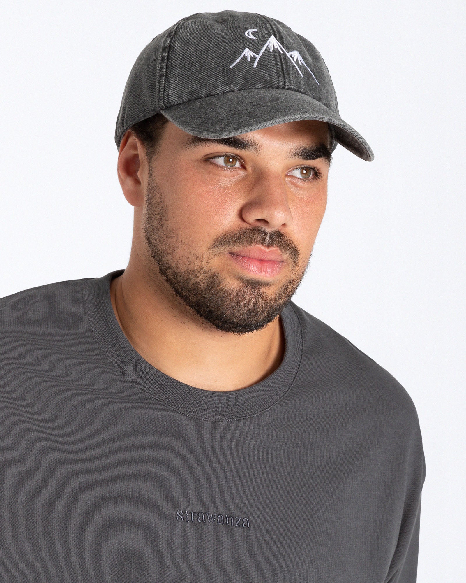 Ein männliches Model trägt eine Bavarian Cap in der Farbe Vintage dunkelgrau mit einem Mond und drei Bergen als Motiv.