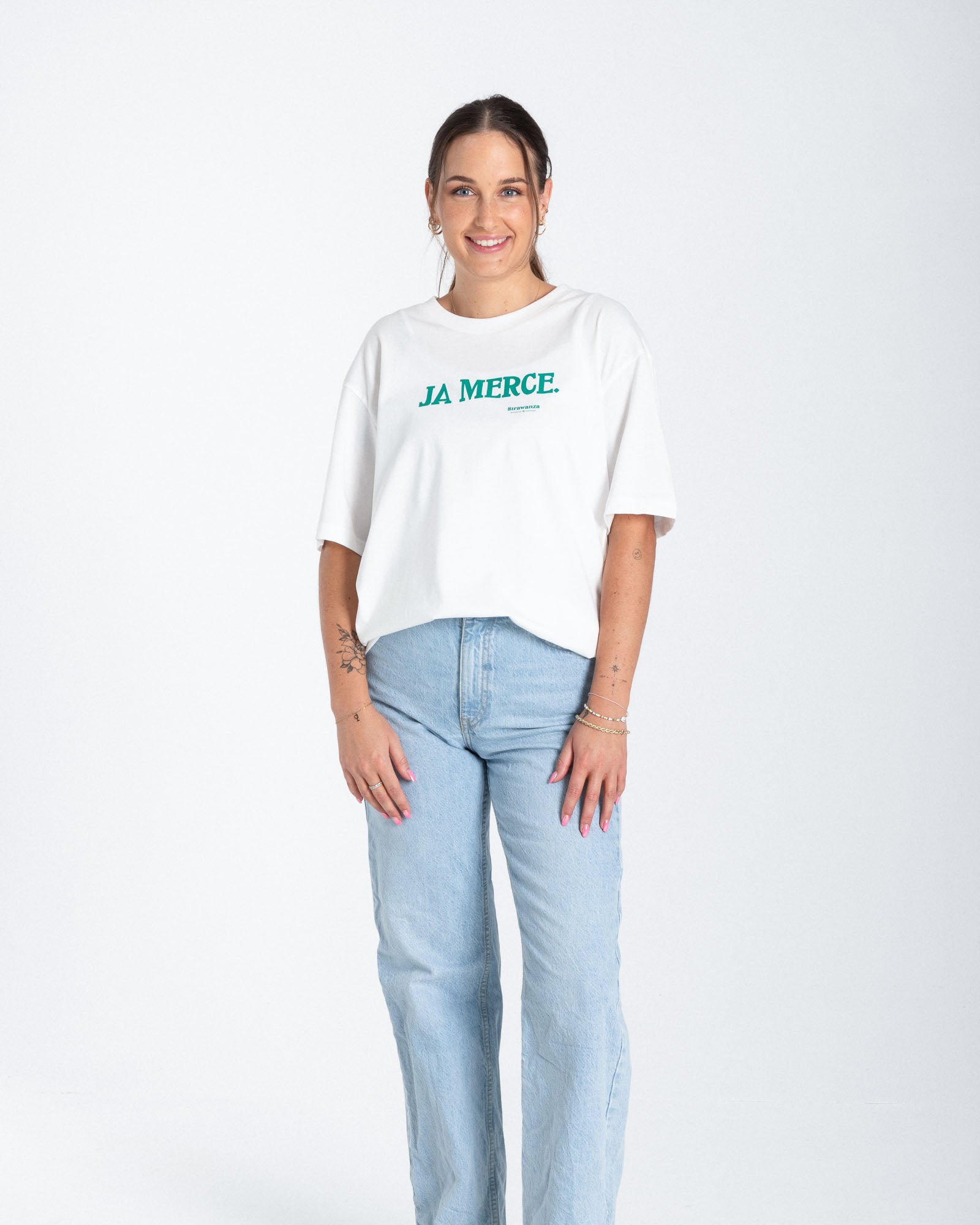 Eine Frau trägt ein weißes T-Shirt mit einem "JA MERCE" Schriftzug in der Farbe dunkelgrün auf der Brusthöhe. 