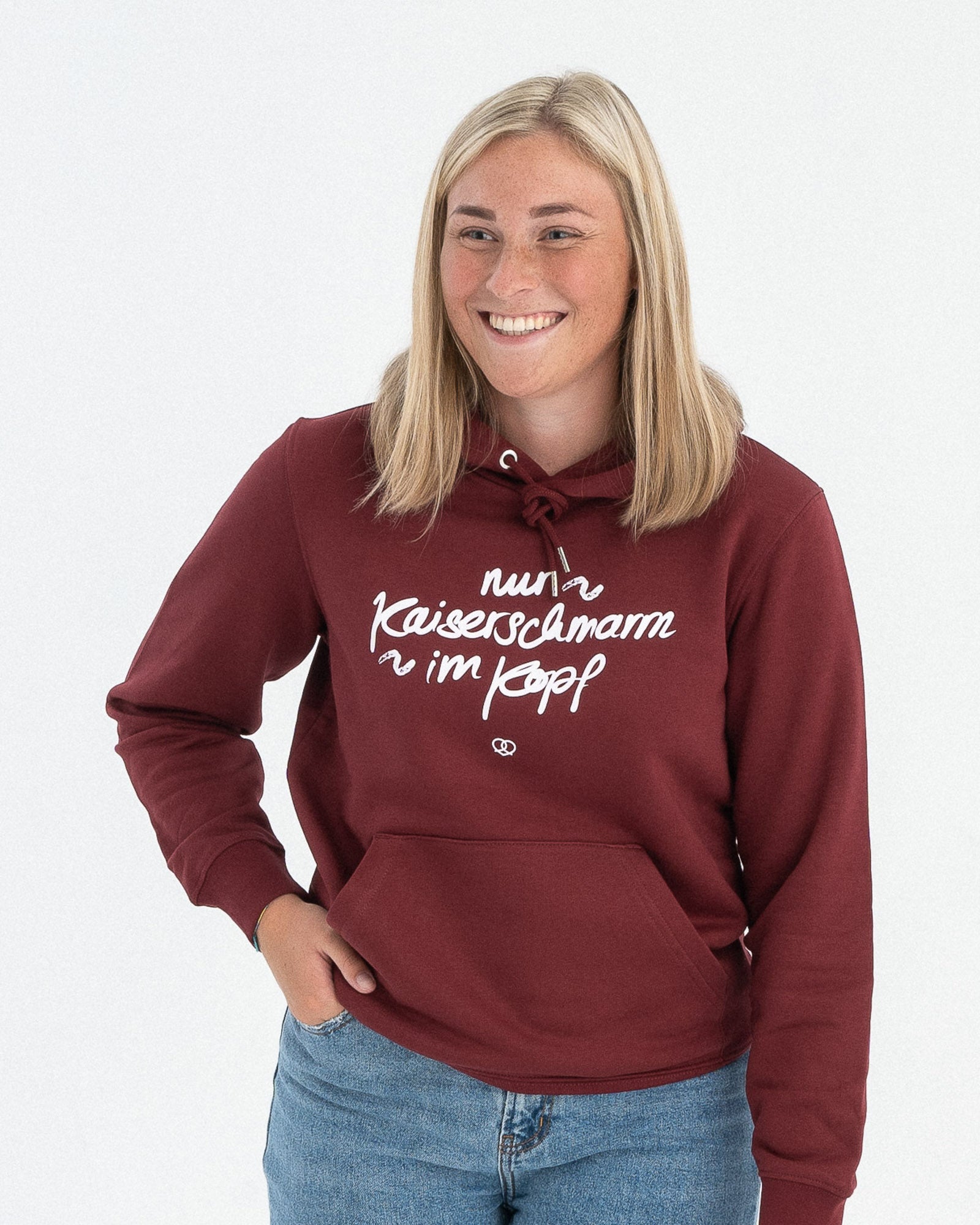 Ein weibliches Model trägt einen weinroten Hoodie mit einem weißen "nur Kaiserschmarrn im Kopf" Schriftzug als Motiv auf der Vorderseite.