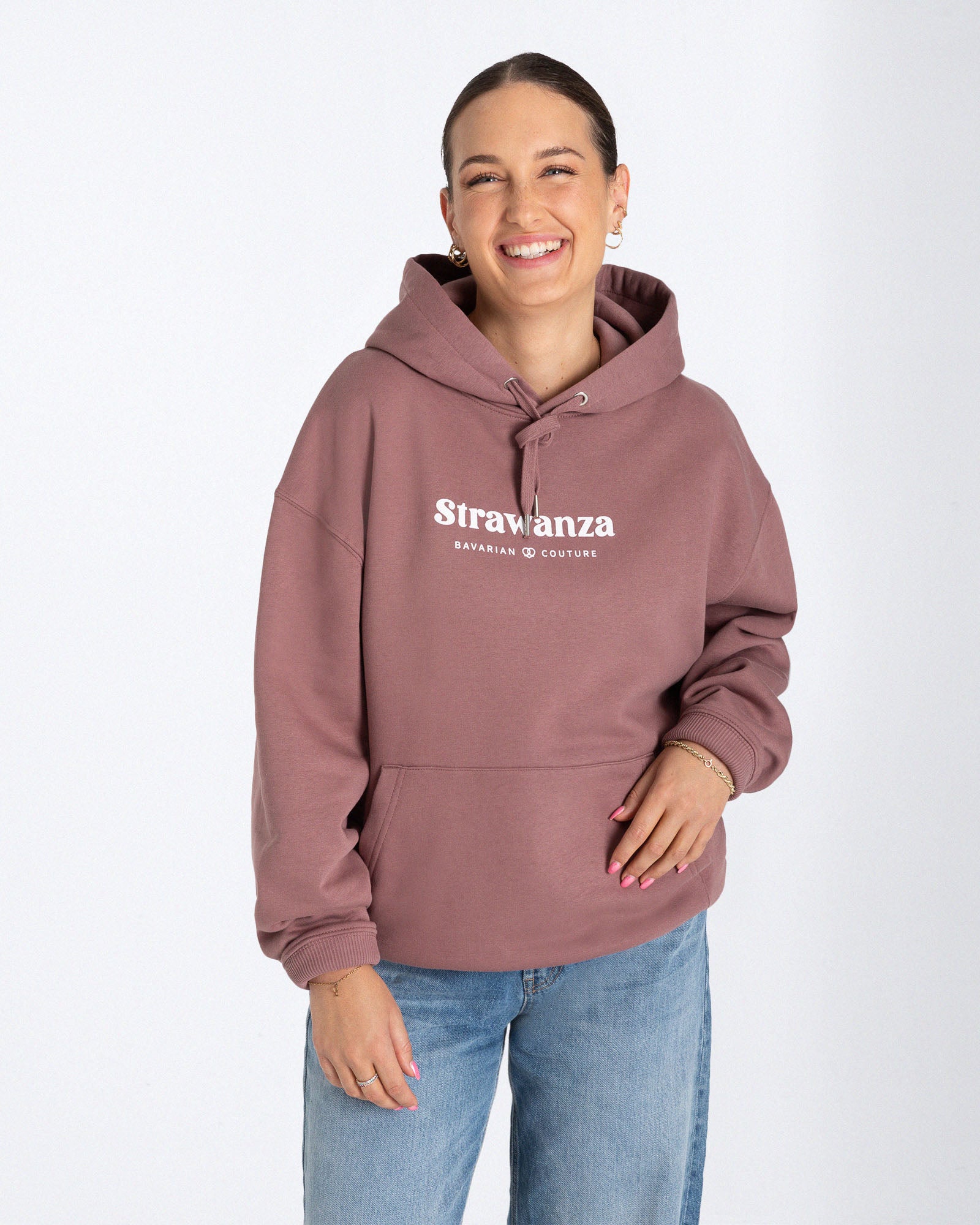 Ein weibliches Model trägt einen rotbraunen Hoodie wo auf der Vorderseite zwei weiße Schriftzüge drauf sind. 