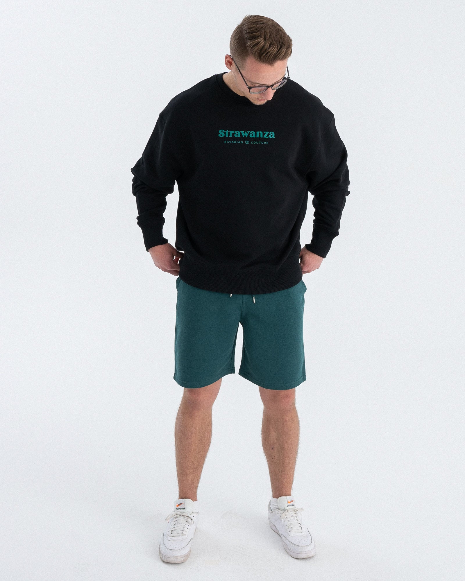 Ein männliches Model trägt einen schwarzen Sweater mit einem in dunkelgrün versehenen "Strawanza" und BAVARIAN COUTURE" Schriftzug auf der Höhe der Brust.